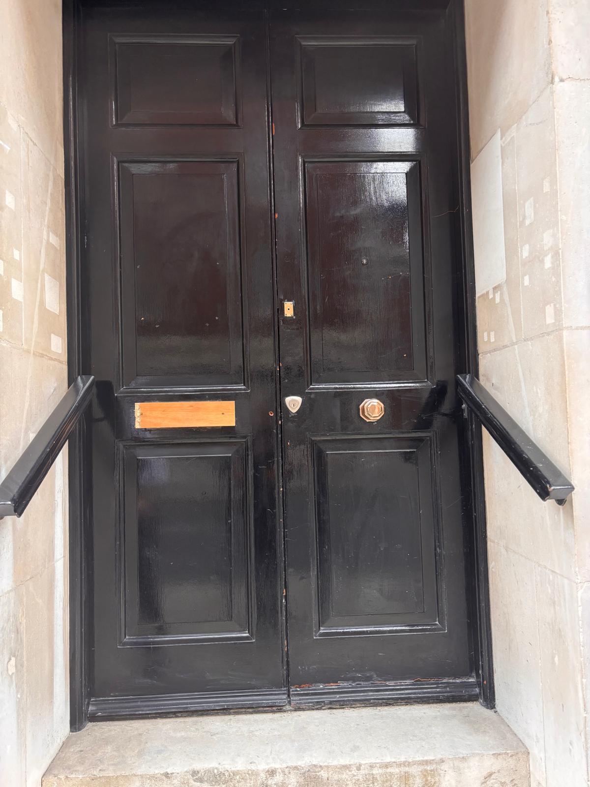 Refurbished communal entrance fire door, North London block — high-gloss black finish on heritage panelled doors in stone surround.